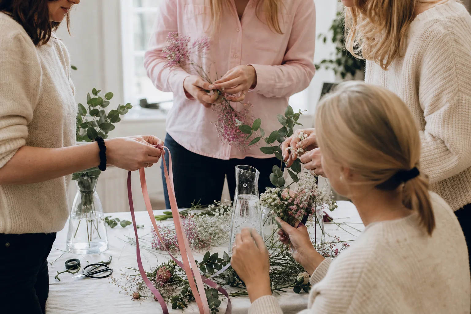 En liten grupp vänner gör blomsterdetaljer vid ett bord i mjukt ljus.