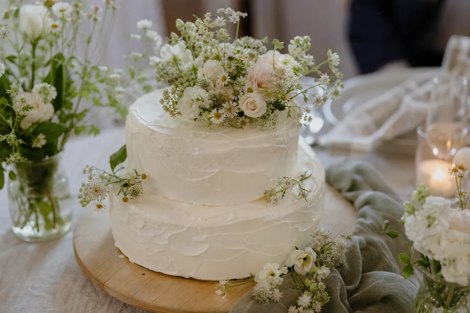 En enkel bröllopstårta står på ett bord med blommor och mjukt ljus utan text.