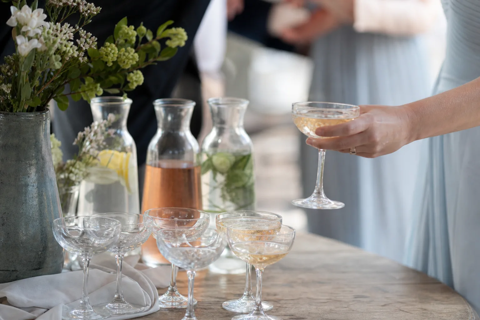 Glas, karaffer och blommor står på ett sidobord utan etiketter eller logotyper.